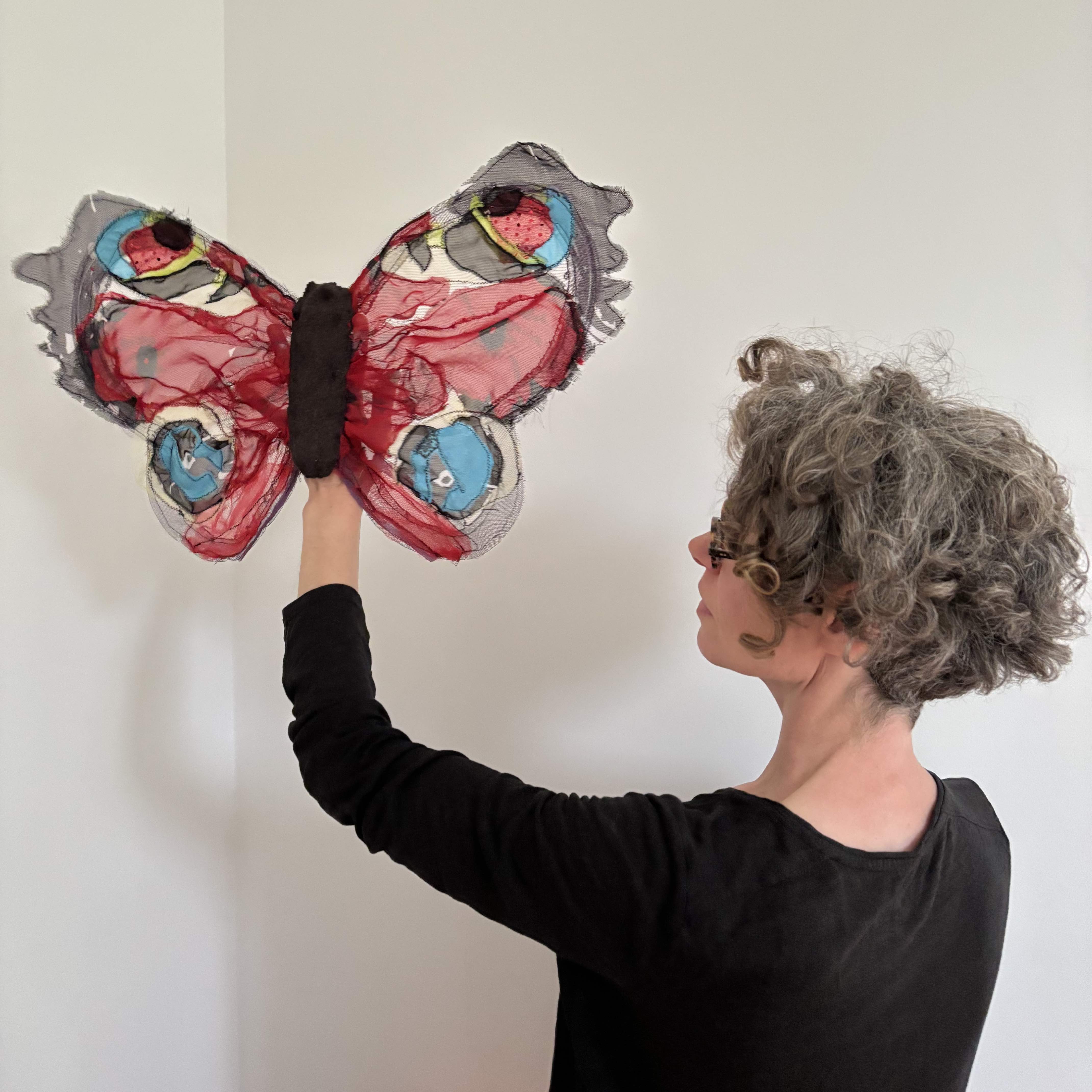 A white, middle-aged woman in black holds up a large peacock butterfly puppet against a white background.